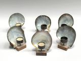 four metal candles are sitting on a wooden stand on a white surface