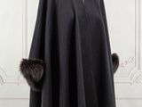 une cape noire à col en fourrure posée sur un présentoir pour mannequin