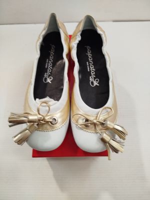 une paire de chaussures blanches ornées de nœuds dorés, posée sur une boîte rouge