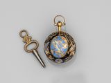 une montre de poche dorée et bleue et une clé posées sur une surface blanche