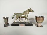 une statue de cheval sur un socle, à côté d'une coupe en argent