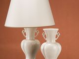 two white vases sitting on a table with a lamp on top of it