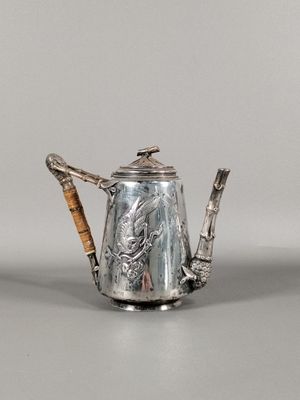 une théière en argent avec une anse en bambou posée sur une table