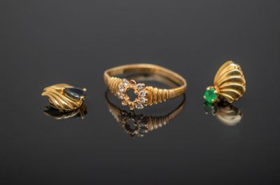 deux bagues en or et une bague ornée de pierres vertes sur un fond noir