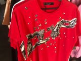 un t-shirt rouge orné d'un serpent, suspendu à un portant dans un magasin de vêtements