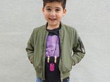a young boy standing in front of a white wall wearing a green jacket