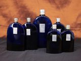 six bouteilles en verre bleues sont alignées en rang sur une table
