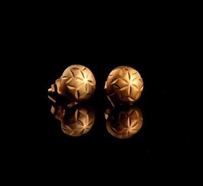 pair of gold earrings on a black surface with reflection