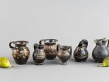 Plusieurs vases et une figurine sont alignés sur une surface grise