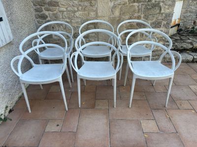 six white plastic chairs sitting in front of a stone wall