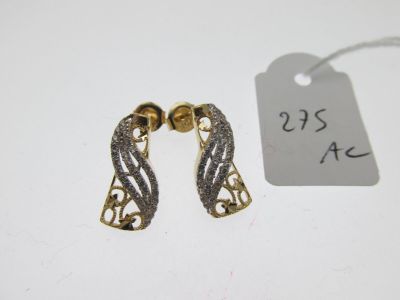 une paire de boucles d'oreilles en or et en argent posées sur une surface blanche