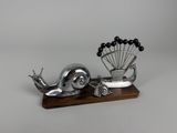 une sculpture en métal représentant un escargot et un paon, posée sur un socle en bois