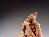 a statue of a man sitting on a rock with a hat on his head