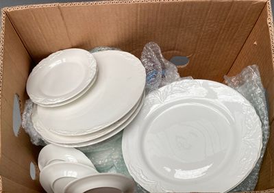 a cardboard box filled with white plates and bowls
