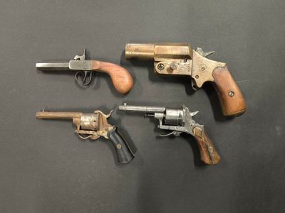 trois vieux revolvers sont posés sur une surface noire et sont munis d'une crosse en bois