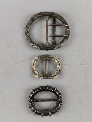 three silver buckles and a silver ring on a white surface