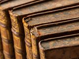 several old books are lined up in a row on a shelf