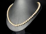 a pearl necklace on a mannequin stand against a black background
