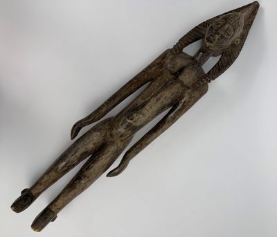 une vieille sculpture en bois représentant un homme tenant un couteau, posée sur une surface blanche