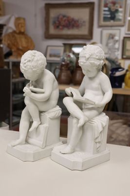 two statues of a boy and a girl sitting on a stool