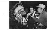 black and white photograph of a man in a native headdress drinking a beer