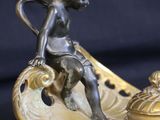 bronze figurine of a boy sitting on a shell with a lid