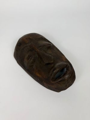 masque en bois sculpté sur une surface blanche, avec un fond blanc