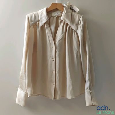 une chemise beige suspendue à un cintre devant un mur blanc
