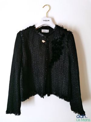 La veste est noire et est ornée d'une fleur.