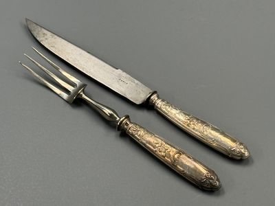 deux couteaux et une fourchette posés sur une table, sur fond gris