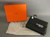 une boîte orange et noire et un sac à main noir posés sur un tissu blanc