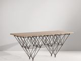 La table est en fil de fer et en bois, avec un plateau en bois.