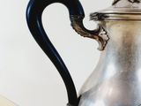 a silver tea pot with a black handle sitting on a table