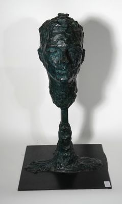 sculpture en bronze représentant une tête, posée sur un socle noir, sur fond blanc