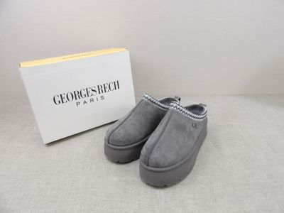 grey sued slippers in front of a white box and a box of shoes