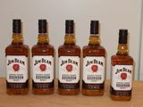 Quatre bouteilles de bourbon sont posées sur une table devant un mur blanc.