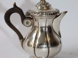 a silver tea pot with a handle on a white surface