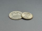 two silver coins sitting on top of each other on a gray surface