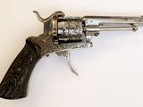 un vieux revolver en argent avec une crosse en bois, posé sur une surface blanche