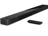 La barre de son est noire et est accompagnée d'une télécommande posée à côté.