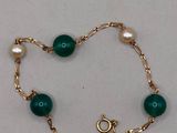 un gros plan sur un bracelet en or orné de perles vertes et de perles de culture