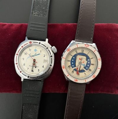two wrist watches sitting on a red velvet cushion