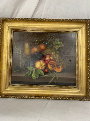 tableau représentant une nature morte aux fruits, dans un cadre doré, posé sur un tissu blanc