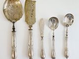 five silver spoons and two silver spoons on a white surface