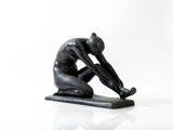 une statue noire représentant un homme à genoux sur une surface blanche