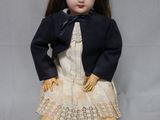 une poupée assise par terre, vêtue d'une robe et d'une veste