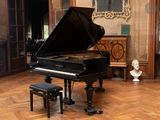a grand piano in the middle of a room with a bust of a man in the background