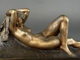 bronze statue of a woman laying on a rock with her hands on her head