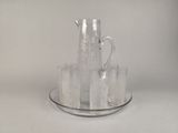 un pichet en verre et quatre verres posés sur une assiette