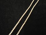un collier de perles blanches avec un fermoir en or sur fond noir